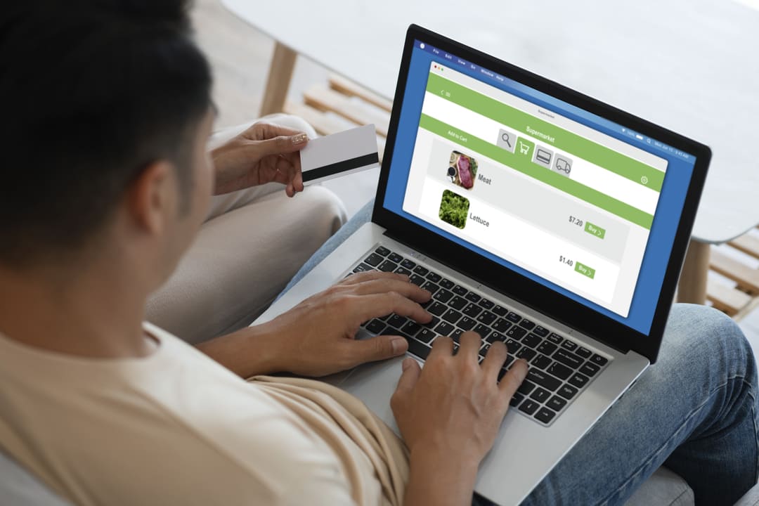 Uma pessoa navegando em uma loja online criada na plataforma Shopify, adicionando seus pedidos ao carrinho de compras, enquanto outra pessoa espera segurando um cartão de crédito.