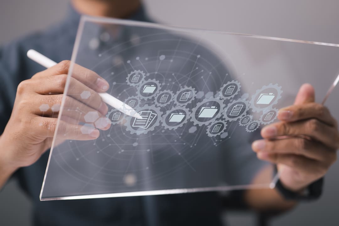 Mãos seguram uma tela de vidro transparente interativa, com ícones digitais de automação, como pastas, documentos e engrenagens, sobrepostos em um fundo tecnológico futurista.