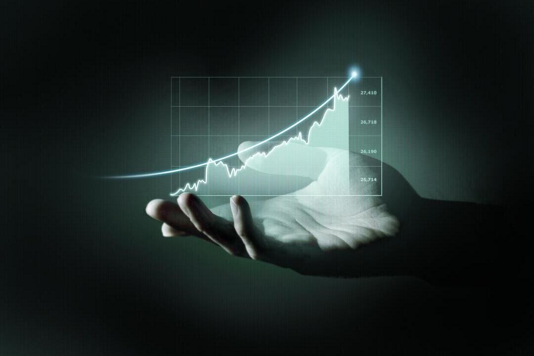 Uma mão aberta em um fundo escuro projeta um holograma com um gráfico de crescimento financeiro. A linha do gráfico tem um formato ascendente, com um ponto luminoso no topo, indicando uma tendência positiva.