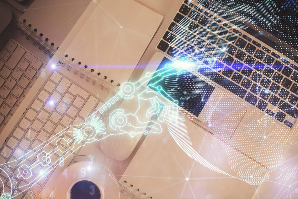 A imagem mostra uma mesa de trabalho com um notebook, teclado externo, cadernos e uma xícara de café. Sobreposta à cena, há uma ilustração translúcida de uma mão robótica feita de circuitos digitais, tocando o teclado. Linhas, números e pontos luminosos sugerem troca de dados e automação. A imagem transmite a ideia de colaboração entre inteligência artificial e trabalho humano em ambientes digitais modernos.