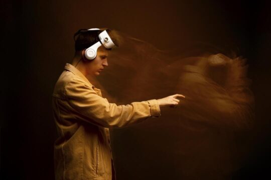 Homem usando headset de realidade virtual em fundo escuro, com efeito de movimento que duplica sua imagem, criando uma sensação de distorção ou alucinação digital.