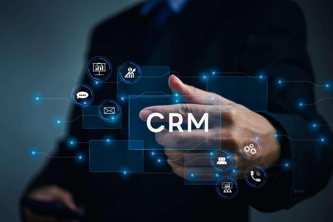 Pessoa em traje formal interagindo com interface virtual onde aparece a sigla "CRM" e ícones relacionados a vendas e relacionamento com o cliente.