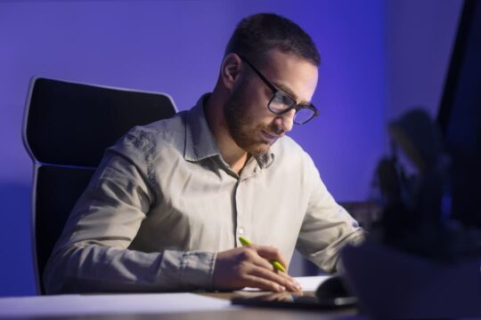 Homem concentrado fazendo anotações em uma mesa de trabalho à noite, representando o processo de planejamento de marketing 2026 em um ambiente corporativo.